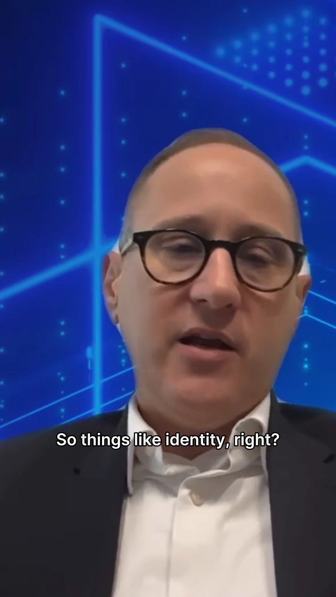A man wearing glasses and a dark suit speaks in front of a blue geometric background with the caption 'So things like identity, right?'