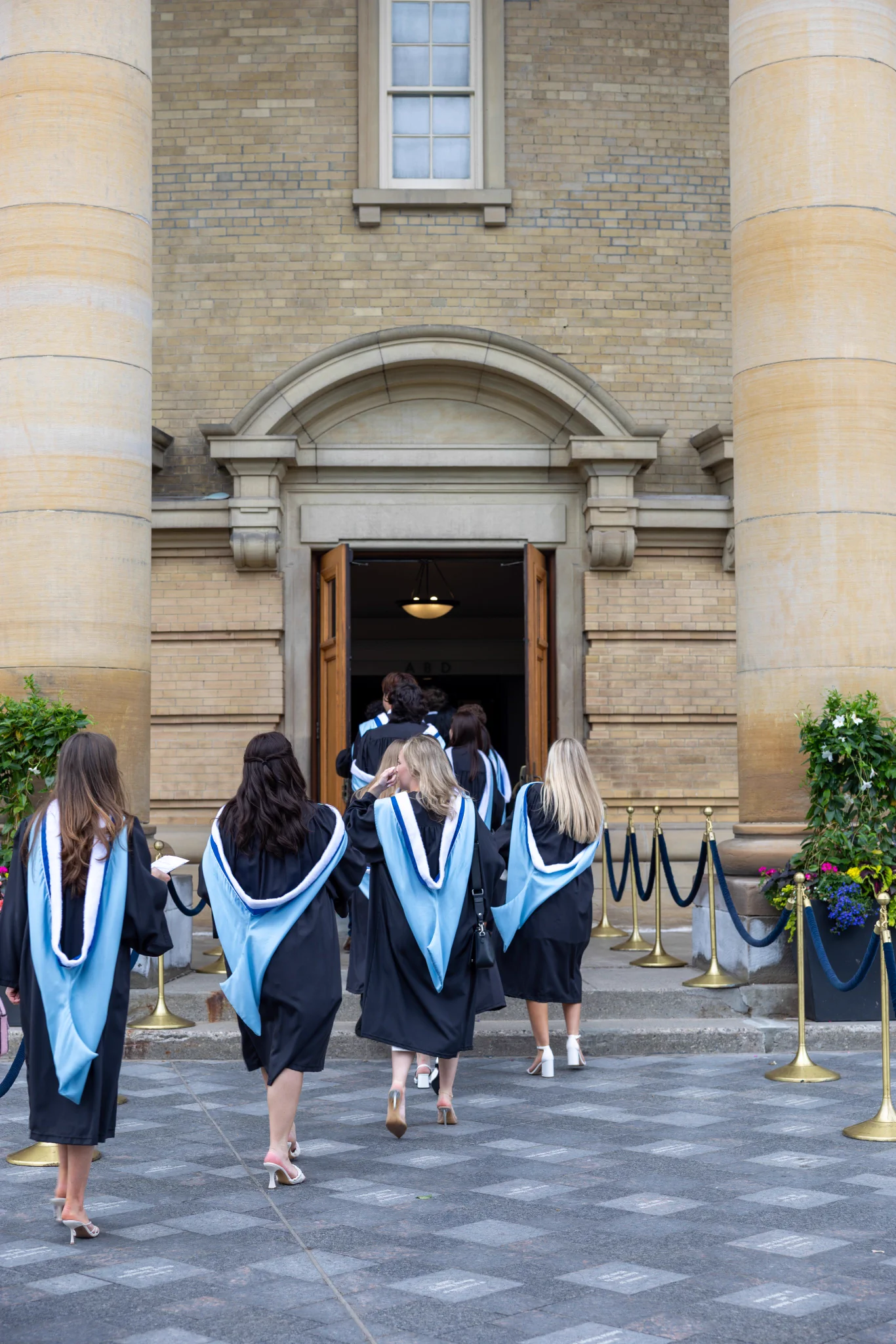 U of T graduates walk into convocation hall wearing gowns and hoods. 