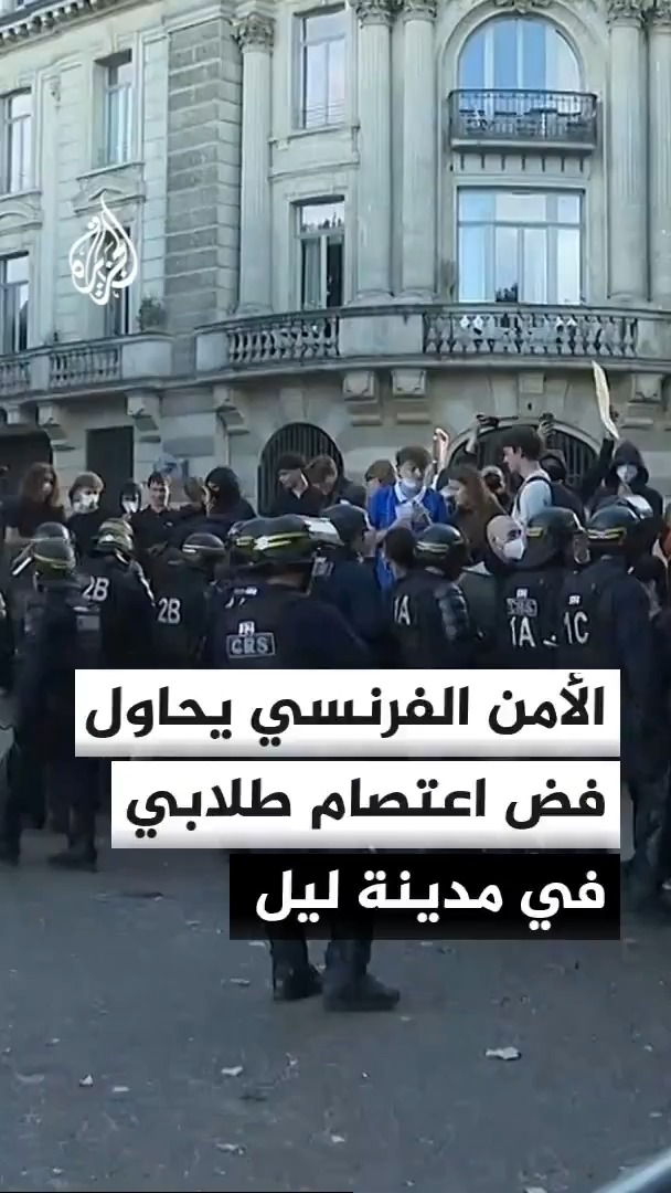 French riot police, identifiable by "CRS" and unit numbers like "2B," "IA," and "IC" on their gear, attempt to disperse a crowd of young protesters outside a classical stone building, with the Al Jazeera (الجزيرة) logo visible above and Arabic text reading "الأمن الفرنسي يحاول فض اعتصام طلابي في مدينة ليل" (French security tries to break up a student sit-in in the city of Lille).
