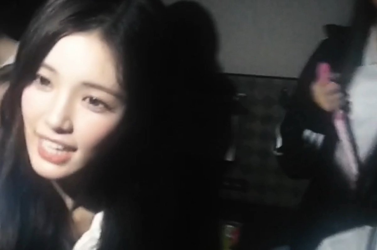 A young woman with long dark hair smiles at the camera in what appears to be a dimly lit indoor setting, possibly a kitchen, with another figure partially visible in the background. The casual selfie-like image likely accompanies the post celebrating the release of "Y - YUHA (feat. Jiwoo)" under the #MILKZZ tag, suggesting the woman pictured is one of the artists involved in the song.