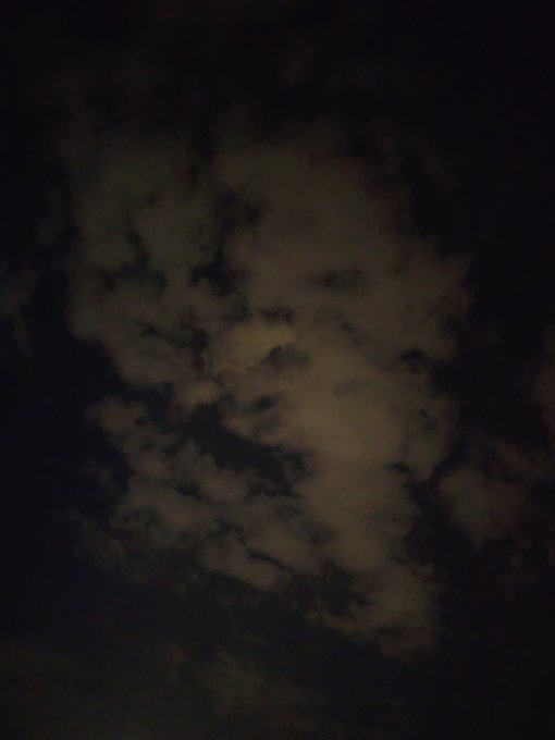 A dark, moody photograph of clouds in a night sky, illuminated faintly with brownish-grey tones.