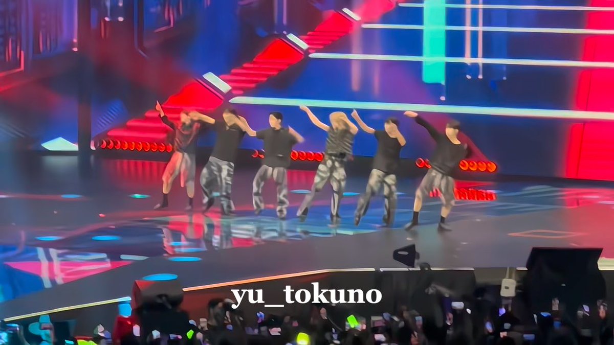 Six performers in dark clothing dance on a brightly lit stage with red and blue lighting; watermark reads 'yu_tokuno'.