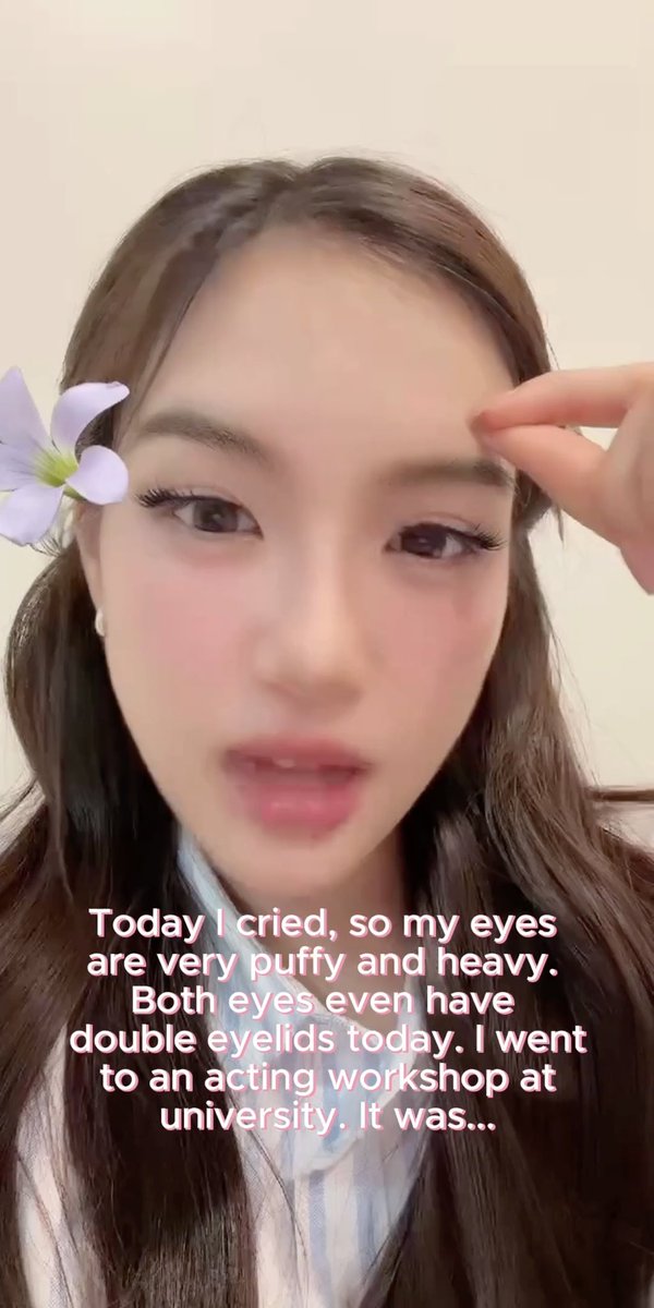 A woman with a purple flower in her hair speaks to camera with text overlay reading: "Today I cried, so my eyes are very puffy and heavy. Both eyes even have double eyelids today. I went to an acting workshop at university. It was..."