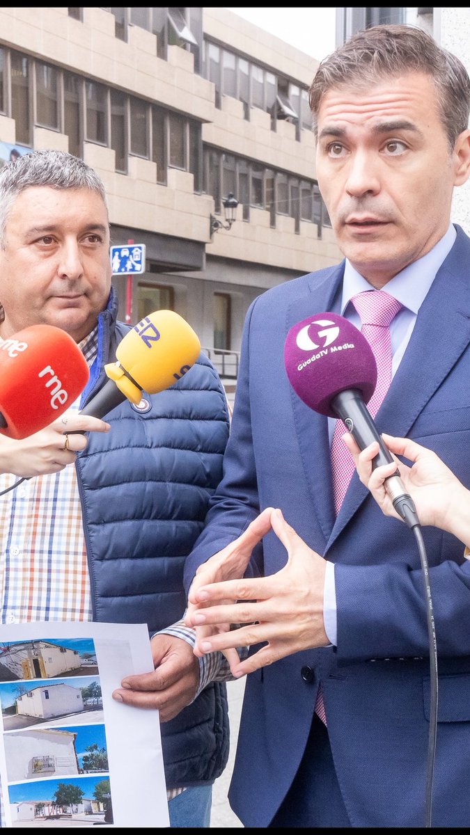 Two men being interviewed outside a building, with microphones from RNE and GuadalTV Media visible, and printed photos of houses being shown.