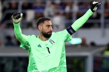 Italian goalkeeper Gianluigi Donnarumma, wearing a green goalkeeper jersey with the number 1, raises his arms during a match.