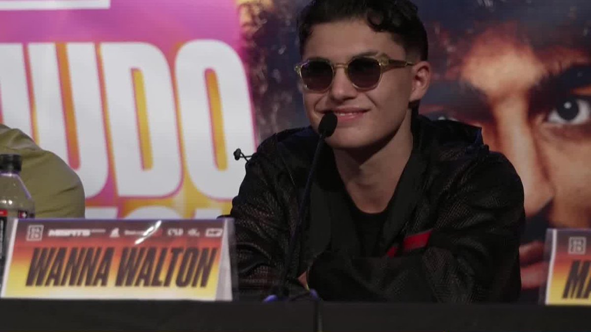 A young man wearing round sunglasses and a black mesh jacket smiles at a press conference, seated behind a microphone with a "WANNA WALTON" nameplate in front of him. The setup supports the post's message about Walton's confidence heading into his September 26 fight against Henry Cejudo on DAZN.