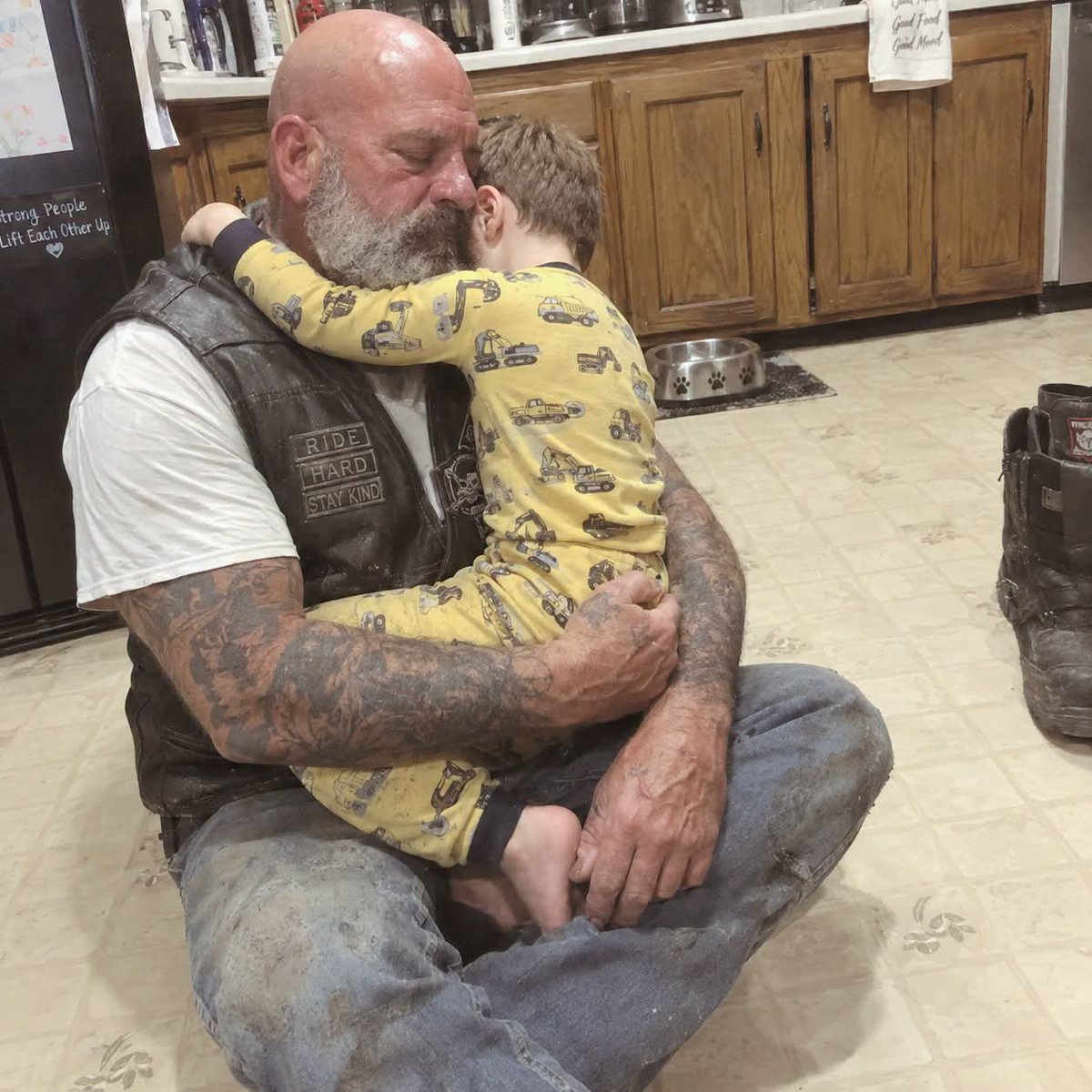 DOGEQEEN's tweet photo. BEAUTIFUL STORY: The Firefighters Called Me To Hold The Boy Who Just Killed His Mother

I'm fifty-four, a biker, both arms sleeved in ink, wearing the same leather cut I've had for three decades. I don't have a counseling license. I'm not a caseworker. No blood relation to anyone involved.

But at three in the morning, dispatch reached out to our motorcycle club's crisis line, and one line pulled me out from under the covers: "We need somebody who won't fall apart. The kid hasn't stopped screaming."

Forty minutes of rain in my face. When I rolled up, there were three fire engines out front, an ambulance behind them, and six firefighters standing on the lawn looking wrecked.

These are guys who charge into buildings that are burning down. Guys who've stood over more bodies than they can count.

Every one of them had tears on his face.

The captain met me at the front step. His hands wouldn't stay still. "The boy's five. Marcus. He smelled smoke, tried to wake his mom up. She told him to run outside and dial 911. He did exactly what she asked."

"She didn't get out?"

"Smoke got her. She pushed him to the door and went down in the hall."

"Where is he?"

"Kitchen. Won't let anybody near him. Keeps repeating that he killed her because he called 911 instead of dragging her out."

I stepped into that kitchen and something inside me came apart.

Marcus was jammed into the corner in yellow pajamas. His face was blotchy and wet. His whole body was shuddering hard enough that I could hear his teeth clicking together. And the same sentences kept spilling out of him.

"I killed my mommy! I was supposed to save her! I killed my mommy!"

I moved toward him slow. No sudden anything. Lowered myself onto the tile maybe three feet away.

He clocked the vest. The ink. My size. The screaming cut off for a second while he took me in.

"Hey, pal. I'm Danny. Gonna hang out right here for a bit. That okay?"

"I killed her," he whispered. "Mommy said go outside and I went and now she's gone and it's because of me."

"Can I tell you something, Marcus? Your mom said go outside because there was nothing on this planet she loved more than you. She needed you out of that house. Getting you through was worth more to her than her own breath."

"But I could've helped!" His voice climbed back to a shriek. "I could've pulled her out! I'm big enough!"

"No, buddy. You couldn't. And your mom knew that. That's the whole reason she sent you. If you'd stayed to help her, there'd be two people gone right now instead of one. She wasn't gonna let that happen."

"But she's dead and I don't have anybody and it's because I didn't save her!"

"Marcus, mind if I tell you something about me?"

He looked at me. Didn't nod. Didn't shake his head. Just looked.

"When I was eight, our house went up too. My dad shook me awake and told me to get out the window and run over to the neighbors. Said he was heading down the hall to grab my baby sister out of her crib."

I stopped for a second. Forty-six years later and telling it still stings.

"I did exactly what my dad said. Went out the window, ran through the yard. Stood there waiting for the two of them to come out." My throat closed for a beat. "They never did, Marcus. The roof came down."

Marcus stared at me. "Your daddy died?"

"And my baby sister. Her name was Emma. She was two."

"Did you think you did it too?"

"For a long time, buddy. I kept thinking maybe if I'd gone back through the window, both of them would still be here. I walked around thinking I was the one who killed them."

"But you were only a kid," Marcus said.

"So are you, pal. So are you."

Something in his face moved. Barely. But it moved.

"Would it be all right if I got closer?" I asked. "I won't touch you unless you want me to. But sitting through this by yourself isn't right."

He didn't answer with words. He threw himself across the tile and into me and mashed his face into my vest and let the crying take him all the way under.

I held on.