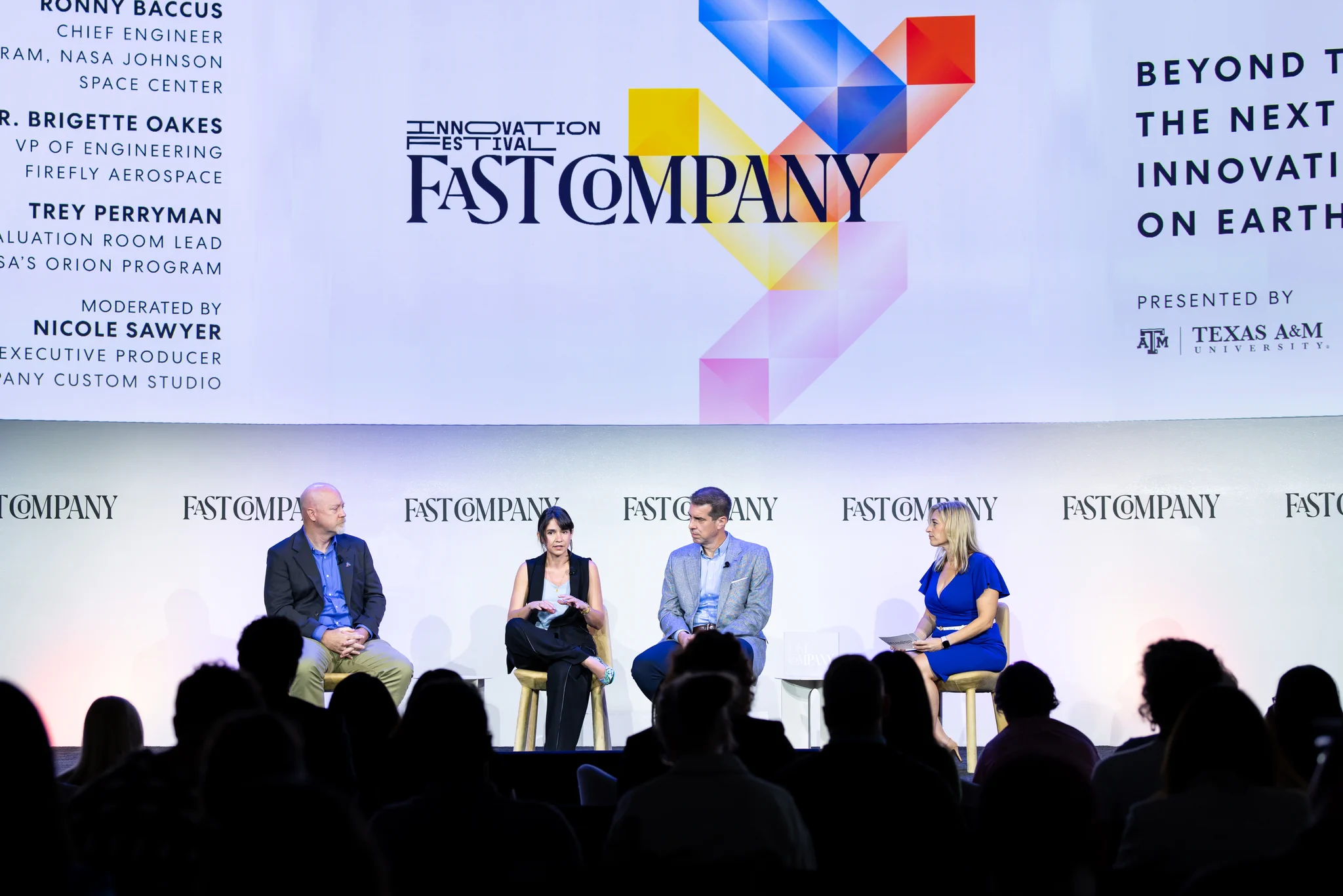The image shows a panel discussion at the Fast Company Innovation Festival. Four individuals are seated on stage, engaged in conversation. The backdrop includes the Fast Company logo and event details. The audience is visible in the foreground.
