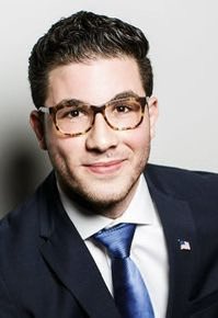 A headshot of Dearborn Mayor Abdullah Hammoud wearing glasses, a dark suit, white shirt, and blue tie, with an American flag pin on his lapel. The image accompanies a post criticizing him over a federal lawsuit alleging unequal treatment of religious groups in city decorations.
