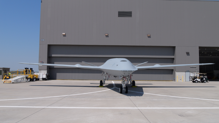 A large gray military-style drone aircraft parked on a tarmac in front of a hangar.