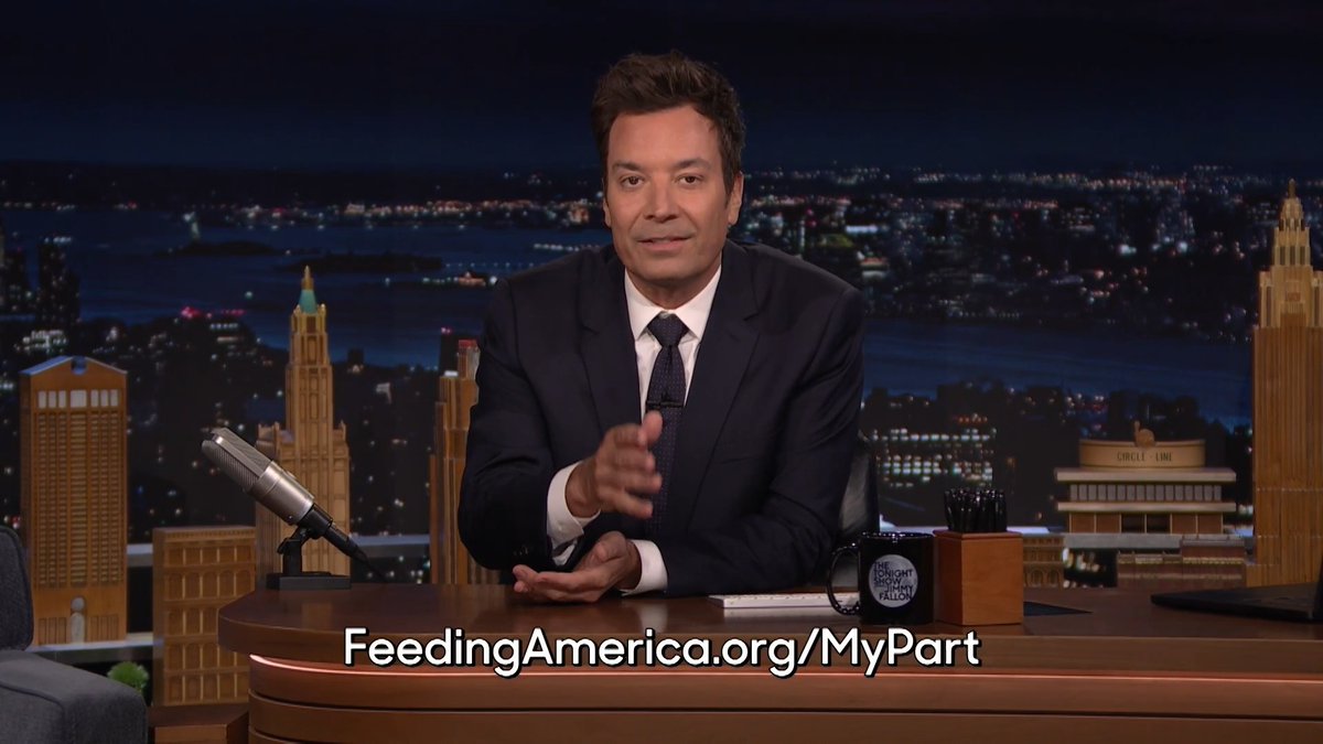 Jimmy Fallon sits at his desk on The Tonight Show with a city skyline backdrop, gesturing toward the camera. The on-screen text reads "FeedingAmerica.org/MyPart," promoting Hunger Action Month and the show's partnership with Feeding America.