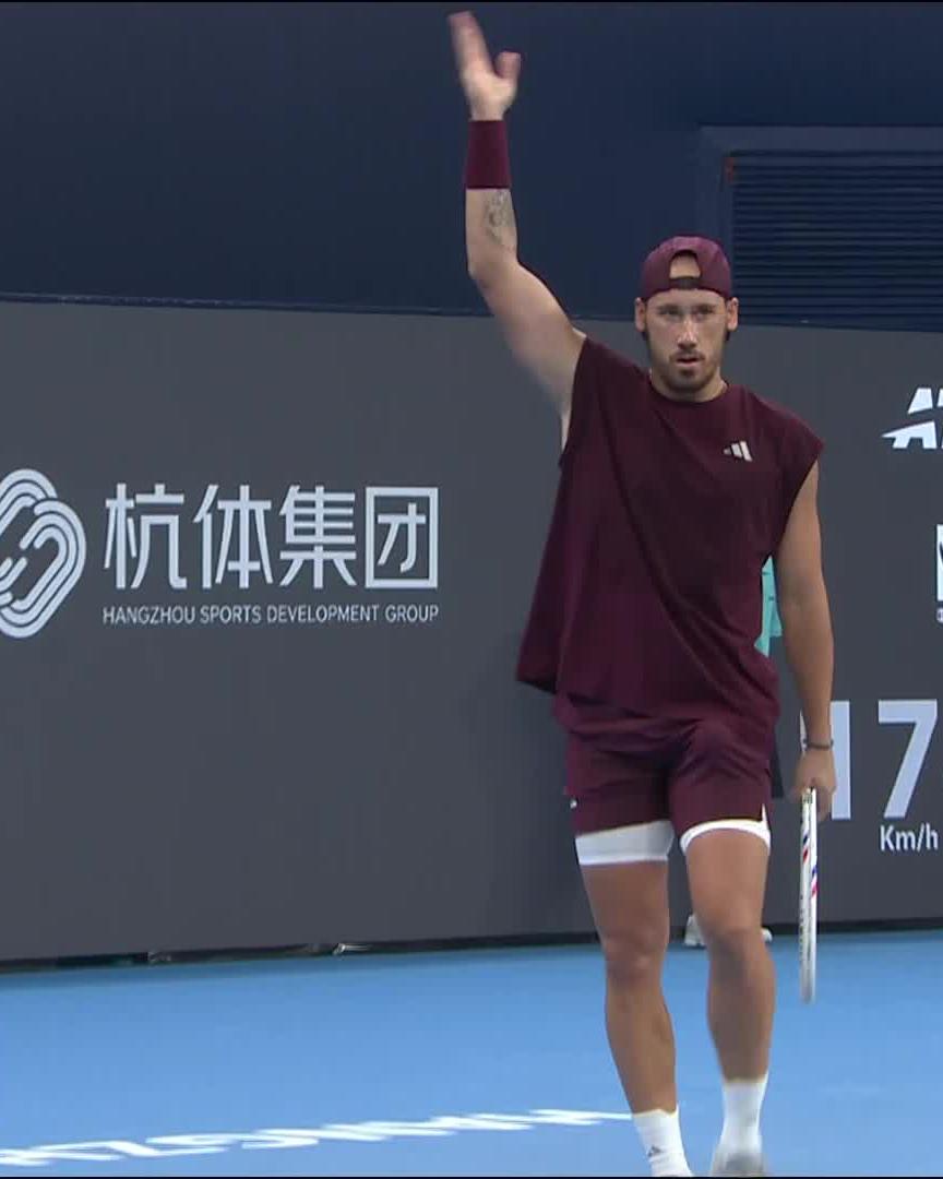 A tennis player in a maroon Adidas outfit waves with his right hand while holding a racket, with the "Hangzhou Sports Development Group" (杭体集团) signage visible in the background, seemingly celebrating a point at the Hangzhou Open. The speed display showing "17 Km/h" likely references the humorous context of Jacquet's improbable lob shot victory.