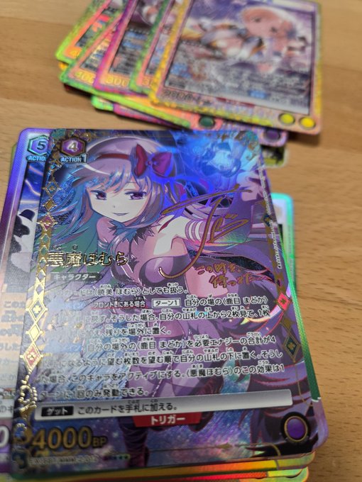 A stack of holographic Japanese trading cards featuring anime-style female characters rests on a wooden surface, with the top card showing '40000' BP.