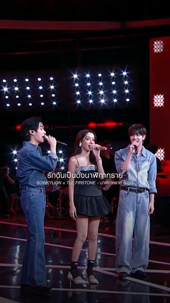 Three performers singing on a stage with bright spotlights in the background, captioned in Thai with 'รักฉันเป็นดั่งมหาพิภัทราย์ BOWKYLION x TLE FIRSTONE - บทพิภัทราย์ (sign)'.