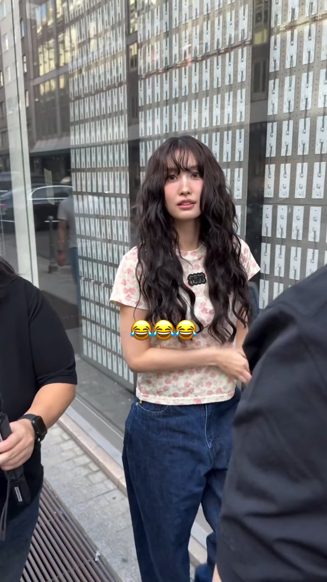 Momo, a K-pop idol, stands outside a building chatting with a fan, likely discussing Italian cuisine like pizza, gelato, pasta, and risotto. Her floral top and long wavy hair complement the casual, candid moment captured on a city street.