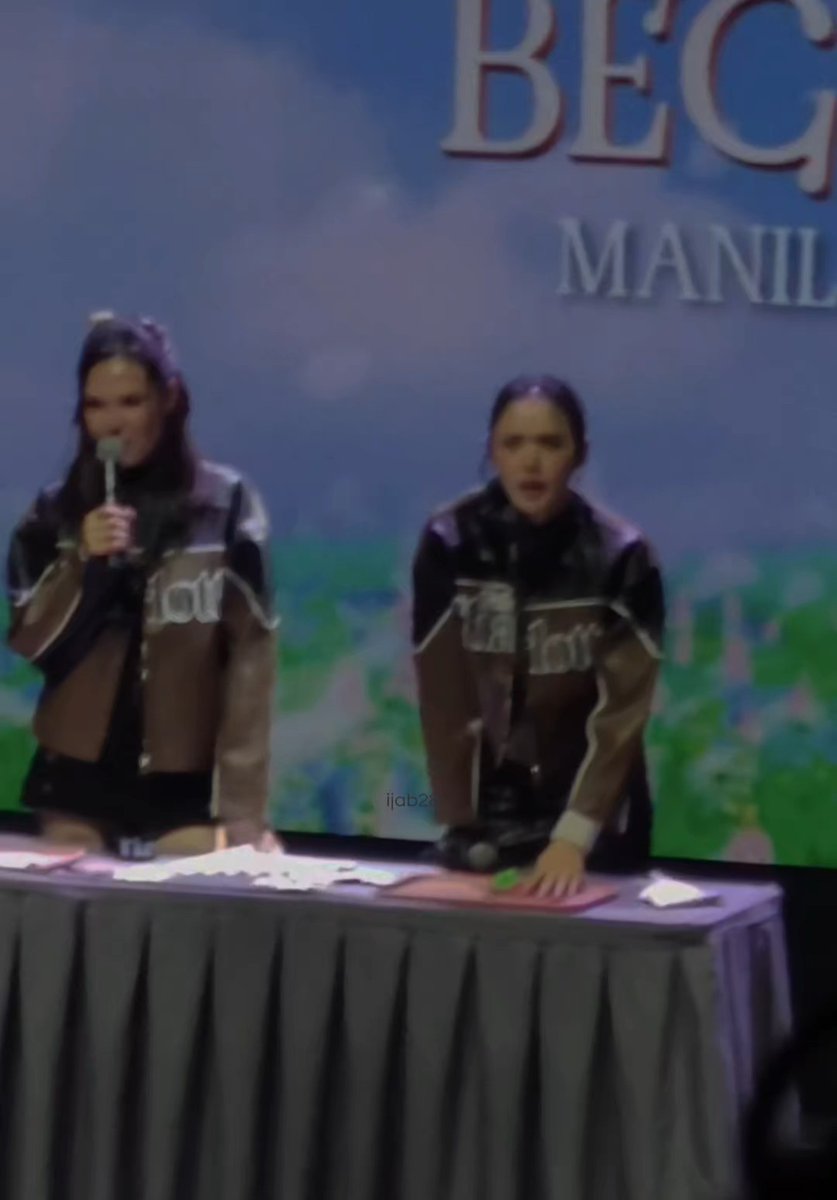 Two women in matching brown 'luv loft' jackets stand at a table during what appears to be a Bigo Live event, with one speaking into a microphone in front of a 'BEGO MANILA' backdrop, watermarked 'ijab25'.