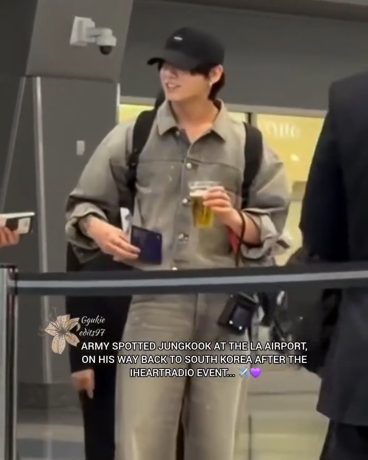 A photo of Jungkook (BTS member) at the airport wearing a black cap and olive-grey shirt, holding a drink; caption reads 'ARMY SPOTTED JUNGKOOK AT THE LA AIRPORT, ON HIS WAY BACK TO SOUTH KOREA AFTER THE IHEARTRADIO EVENT... ✈️💜' with watermark '@gukie_edits97'.