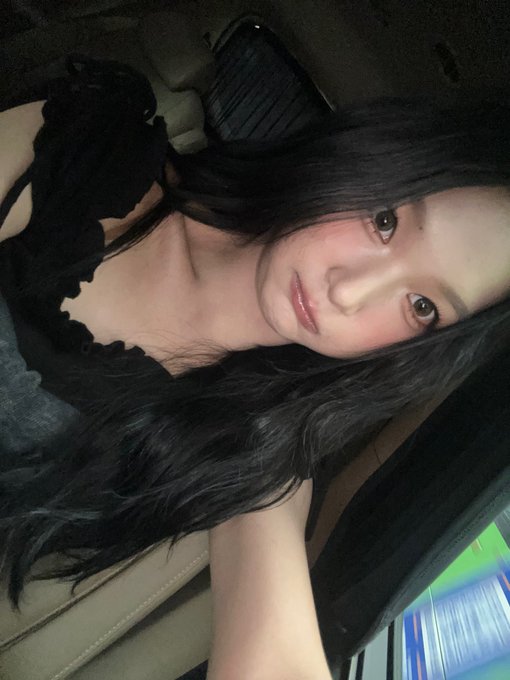 A close-up selfie of a young woman with long black hair sitting inside a car, looking directly at the camera.