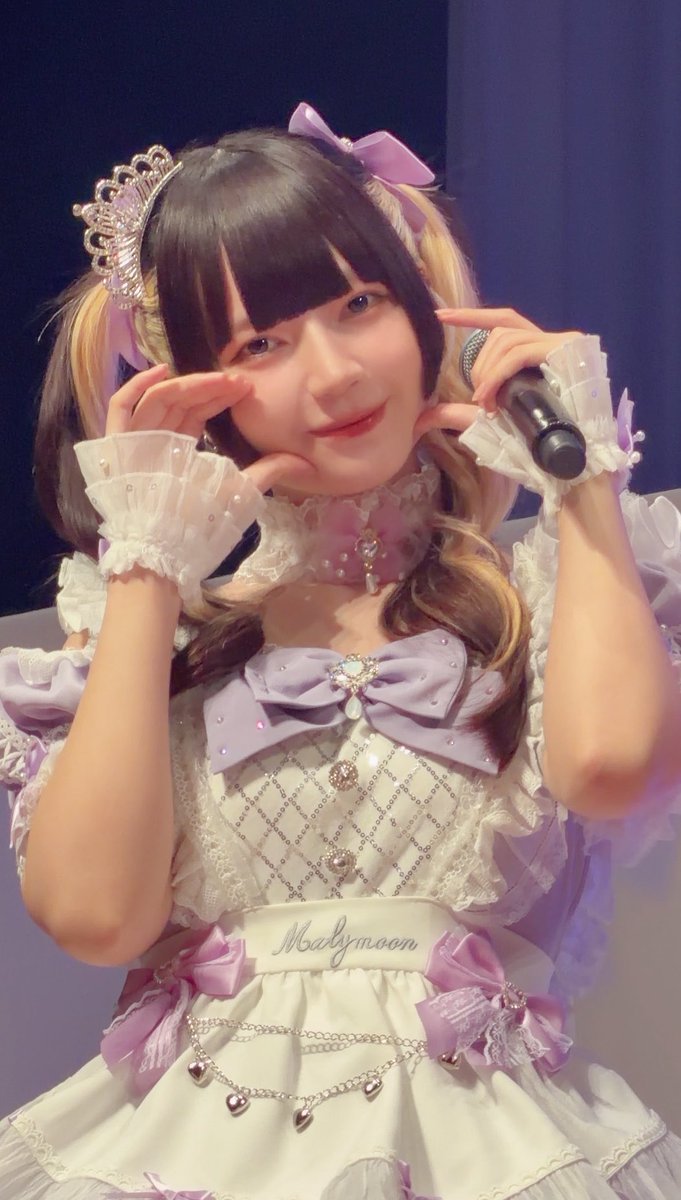 A young woman in an ornate lavender and white frilly idol costume with a "Malymoon" sash poses playfully with her hands framing her face while holding a microphone, wearing a small tiara and hair bows. The post "やねちゃんの10秒間" (Yane-chan's 10 seconds) suggests this is a brief performance moment captured during a stage appearance.