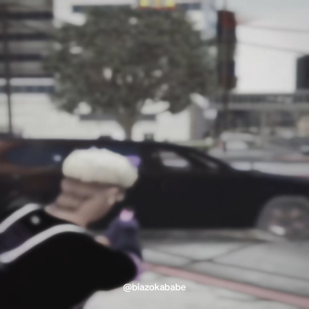 A blurry photo showing a person with white hair in the foreground, with a black car and a tree visible in the background in what appears to be a video game or virtual environment. The watermark "@blazokababe" appears at the bottom.