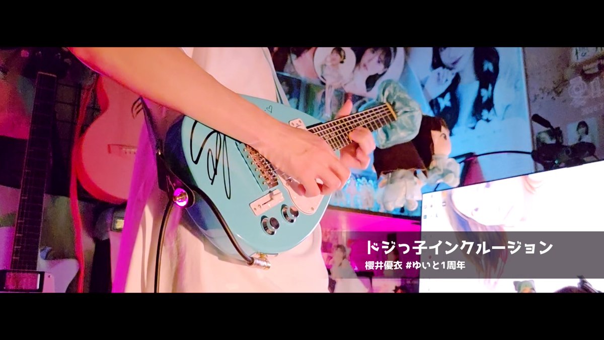 A person plays a light blue electric guitar in a room decorated with anime posters and plush toys, with Japanese text 'ドジっ子インクルージョン 櫻井優衣 #ゆいど1周年' overlaid.