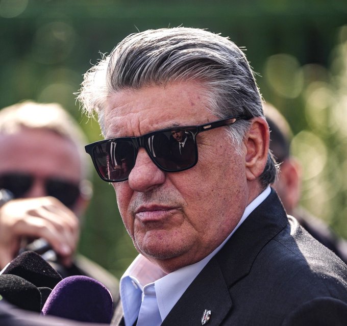 Serdal Adali, a Turkish sports official, wears dark sunglasses while speaking to reporters with microphones in front of him. His statement highlights his concerns about referee errors disproportionately affecting major Turkish football clubs like Beşiktaş, Trabzonspor, Fenerbahçe, and Rizespor, suggesting deliberate provocation of their fan bases.
