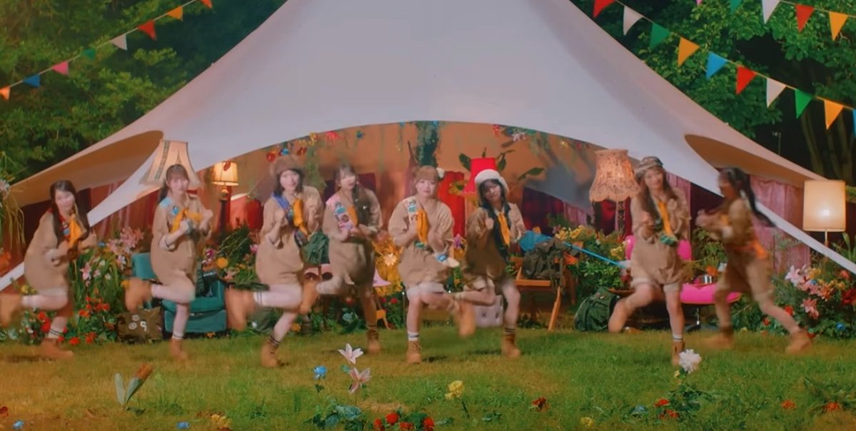 Nine young women in scout-themed outfits perform a synchronized dance routine in front of a large white tent decorated with colorful bunting and floral arrangements, matching the post's enthusiastic praise of the choreography from Kyunsto (きゅーすと).