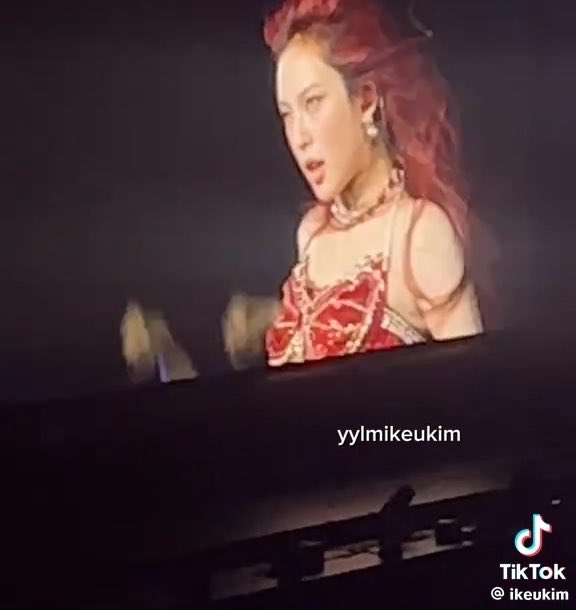 A fan captures Chiquita from BABYMONSTER performing her solo "Worth It" on what appears to be a large screen or display, with the TikTok watermark "@ikeukim" and "yylmikeukim" visible. The clip aligns with the post, showing her dramatic red outfit and expressive performance that prompted an enthusiastic reaction from a Japanese fanboy.
