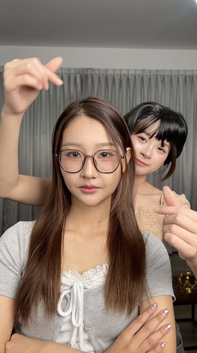 Two young women pose playfully for a selfie in front of gray curtains, one making a peace sign above her head while the other peeks from behind making a thumbs-up, with their hashtag-filled post highlighting CGM48 members and a "face-changing show" theme.