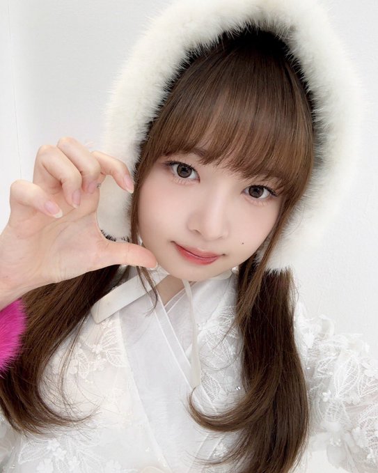 Close-up selfie of a young woman with long brown hair wearing a fluffy white hooded jacket and white lace top, posing with her hand near her face.