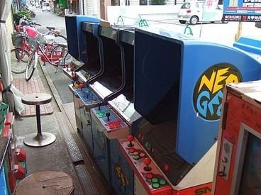 b_wings1234's tweet photo. かつて、世界はアーケードゲームに満ちていた。

ゲームセンター以外にも、街のあちこちにアーケードゲーム(※)が置かれていた。

今回はそんな「街角アーケードゲーム」について書いていきたい。
※この投稿ではビデオゲームを指します

例えばスペースインベーダーのブームの時には多くの喫茶店に
筐体が置かれ、ブームが去った後も筐体を置き続けた店もあった。

私が子供の頃、自宅近くの喫茶店にパックマンが置いてあり、窓から見えるパックマンのデモ画面に心奪われて窓越しにジーッと見ていたら、あっちに行きなさいとマスターにたしなめられたことを覚えている(笑)

そして街角にあるアーケードゲームの代表格と言えば駄菓子屋だ。ゲームセンターに行くことが出来ない子供たちにとって、駄菓子屋の筐体は大きな味方だった。あのオレンジ筐体でアーケードゲームを初めて体験したという方も多いと思う。

おもちゃ屋の中に筐体が置かれているというケースもあった。おもちゃ屋も子供たちが集まる場所であり、駄菓子屋と似たようなパターンと言えるかもしれない。

例えば私が通っていたおもちゃ屋はスペースの問題から台数は少なかったが、店主のセンスが良く、選りすぐりのゲームが入荷していた。

マイベストゲームであるリブルラブルと衝撃的な出会いをしたのもそこだったし、友人たちとドルアーガの塔を初めてクリアしたのもそのおもちゃ屋だった。

残念ながらもうそのおもちゃ屋は存在していないが、そこでのゲーム体験は強烈で、私は今もそのおもちゃ屋の中の様子をありありと思い出すことが出来る。

デパートの屋上や大型のスーパーマーケットのゲームコーナーにも、当然のようにアーケードゲームが並んでいた。ゲームセンターよりも比較的安全にゲームが出来るので、重宝していた方もいたのではないだろうか。

しかし80年代も後半になると、街角アーケードゲームもゲームの多様化や家庭用機の台頭と共に数を減らしていくのだが、90年代に入ると強力な救世主が現れる。

MVS(NEOGEO)筐体である。

比較的安価で設置することが出来たMVS筐体は、対戦格闘ゲームのブームをきっかけに爆発的に普及し、街のあちこちで見かけるようになった。

これまで紹介した場所以外にも、書店・文房具店・酒屋・コンビニ・パン屋・米屋・自動車教習所の待合室などなど…。それは私が80年代に体験した以上の密度だった。

ゲームセンターという「点」での展開になりがちだったアーケードゲームが、街の様々な店舗にも置かれることで点が結ばれ、「面」での展開が実現した。この事象は、もしかしたらインベーダープーム以来のことだったのかもしれない。

MVS(NEOGEO)の勢いは海外にも飛び火し、特に中南米では凄まじい勢いで普及していった。メキシコの小さな商店に置かれたMVSで、子どもがNEOGEOのゲームに興じている写真を見たことがある。

日本から1万キロも距離が離れていても、同じようなゲーム体験を共有できていたのだと思うと、何だか温かい気持ちになった。

一方日本では、街の至る所にあったMVS筐体も対戦格闘ブームの終焉やSNKの倒産、そしてゲームセンター自体の減少と共に急激に数を減らしていき、今では街角アーケードゲームは絶滅に近い状態にある。

家庭用ゲーム機がアーケードゲームの性能を追い抜き、高品質のゲームを家でいつでも楽しめるようになったのだから、それも当然と人は言う。

分かる、道理が通っている。が…。

今振り返ると、当時家では出来なかったゲームをプレイ出来るということ以上に、街角でアーケードゲームをプレイするという体験そのものが特別なことだったのかもしれないと思うのだ。

ゲーセンより小さいけど、家でも学校でもないコミュニティがあった場所。
開放的で、人の目が届く安全な場所でのゲームプレイ。
外にいても、ふと筐体を見かければ遊べる即時性。

街角アーケードゲームには、そういう役割もあったのではないか。

街角という日常と地続きの場所で、ちょっとした非日常を体験できる。そんなゲーム体験そのものに、価値があったのだと私は思うのである。
#レトロゲーム