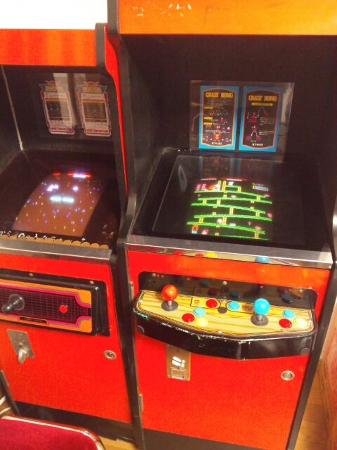 b_wings1234's tweet photo. かつて、世界はアーケードゲームに満ちていた。

ゲームセンター以外にも、街のあちこちにアーケードゲーム(※)が置かれていた。

今回はそんな「街角アーケードゲーム」について書いていきたい。
※この投稿ではビデオゲームを指します

例えばスペースインベーダーのブームの時には多くの喫茶店に
筐体が置かれ、ブームが去った後も筐体を置き続けた店もあった。

私が子供の頃、自宅近くの喫茶店にパックマンが置いてあり、窓から見えるパックマンのデモ画面に心奪われて窓越しにジーッと見ていたら、あっちに行きなさいとマスターにたしなめられたことを覚えている(笑)

そして街角にあるアーケードゲームの代表格と言えば駄菓子屋だ。ゲームセンターに行くことが出来ない子供たちにとって、駄菓子屋の筐体は大きな味方だった。あのオレンジ筐体でアーケードゲームを初めて体験したという方も多いと思う。

おもちゃ屋の中に筐体が置かれているというケースもあった。おもちゃ屋も子供たちが集まる場所であり、駄菓子屋と似たようなパターンと言えるかもしれない。

例えば私が通っていたおもちゃ屋はスペースの問題から台数は少なかったが、店主のセンスが良く、選りすぐりのゲームが入荷していた。

マイベストゲームであるリブルラブルと衝撃的な出会いをしたのもそこだったし、友人たちとドルアーガの塔を初めてクリアしたのもそのおもちゃ屋だった。

残念ながらもうそのおもちゃ屋は存在していないが、そこでのゲーム体験は強烈で、私は今もそのおもちゃ屋の中の様子をありありと思い出すことが出来る。

デパートの屋上や大型のスーパーマーケットのゲームコーナーにも、当然のようにアーケードゲームが並んでいた。ゲームセンターよりも比較的安全にゲームが出来るので、重宝していた方もいたのではないだろうか。

しかし80年代も後半になると、街角アーケードゲームもゲームの多様化や家庭用機の台頭と共に数を減らしていくのだが、90年代に入ると強力な救世主が現れる。

MVS(NEOGEO)筐体である。

比較的安価で設置することが出来たMVS筐体は、対戦格闘ゲームのブームをきっかけに爆発的に普及し、街のあちこちで見かけるようになった。

これまで紹介した場所以外にも、書店・文房具店・酒屋・コンビニ・パン屋・米屋・自動車教習所の待合室などなど…。それは私が80年代に体験した以上の密度だった。

ゲームセンターという「点」での展開になりがちだったアーケードゲームが、街の様々な店舗にも置かれることで点が結ばれ、「面」での展開が実現した。この事象は、もしかしたらインベーダープーム以来のことだったのかもしれない。

MVS(NEOGEO)の勢いは海外にも飛び火し、特に中南米では凄まじい勢いで普及していった。メキシコの小さな商店に置かれたMVSで、子どもがNEOGEOのゲームに興じている写真を見たことがある。

日本から1万キロも距離が離れていても、同じようなゲーム体験を共有できていたのだと思うと、何だか温かい気持ちになった。

一方日本では、街の至る所にあったMVS筐体も対戦格闘ブームの終焉やSNKの倒産、そしてゲームセンター自体の減少と共に急激に数を減らしていき、今では街角アーケードゲームは絶滅に近い状態にある。

家庭用ゲーム機がアーケードゲームの性能を追い抜き、高品質のゲームを家でいつでも楽しめるようになったのだから、それも当然と人は言う。

分かる、道理が通っている。が…。

今振り返ると、当時家では出来なかったゲームをプレイ出来るということ以上に、街角でアーケードゲームをプレイするという体験そのものが特別なことだったのかもしれないと思うのだ。

ゲーセンより小さいけど、家でも学校でもないコミュニティがあった場所。
開放的で、人の目が届く安全な場所でのゲームプレイ。
外にいても、ふと筐体を見かければ遊べる即時性。

街角アーケードゲームには、そういう役割もあったのではないか。

街角という日常と地続きの場所で、ちょっとした非日常を体験できる。そんなゲーム体験そのものに、価値があったのだと私は思うのである。
#レトロゲーム