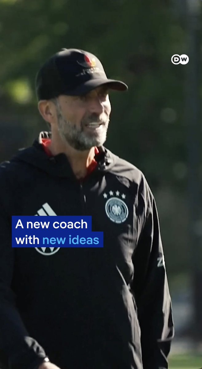 A man with a gray beard wearing a black cap and German national team jacket, with text overlay reading "A new coach with new ideas" and a DW logo.