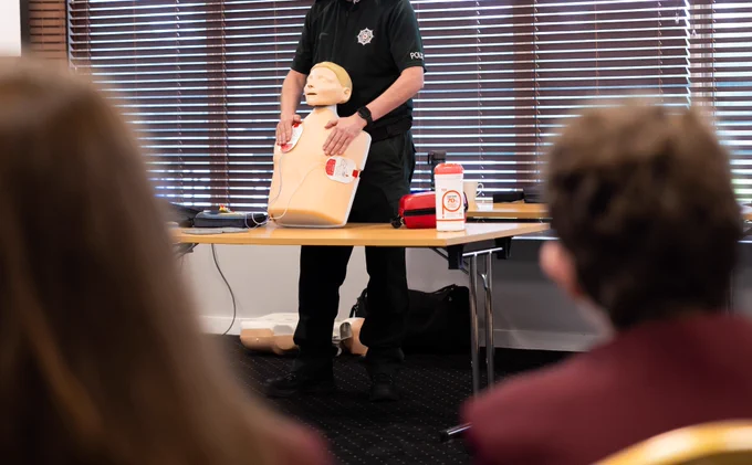 A police officer demonstrates how to use an AED on a CPR mannequin during a first aid training session.