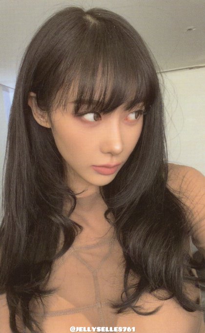 A close-up selfie of a young woman with long dark wavy hair and bangs, wearing a sheer orange top, with the watermark '@JELLYBELLE761' at the bottom.