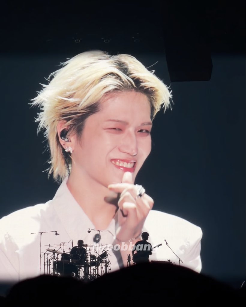 A person with shaggy blonde hair and red-tinted contact lenses smiles and winks while holding a microphone on stage, with a "weverse" watermark visible. The caption "My eyes got so dry that I didn't even realize I was wearing lenses" humorously references the visible red irritation in their eyes, joking that they're so focused on the performance they forgot about the contact lenses causing discomfort.