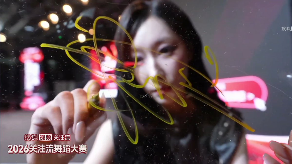 A woman draws yellow squiggly lines on a glass surface, with Chinese text '搜狐视频 关注流' and '2026关注流舞蹈大赛' (Sohu Video Attention Flow 2026 Dance Competition) in the bottom left.