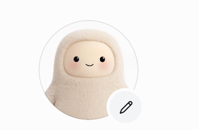 A cute plush character with a smiling face wearing a beige hooded outfit, featuring an edit pencil icon in the corner.