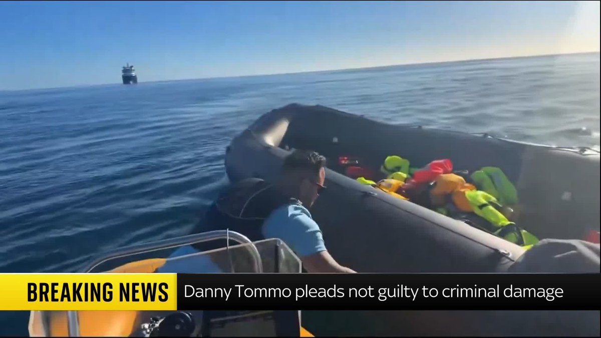 An inflatable boat carries people in high-visibility life jackets across the English Channel, with a larger vessel visible in the distance. A "BREAKING NEWS" banner reads: "Danny Tommo pleads not guilty to criminal damage."