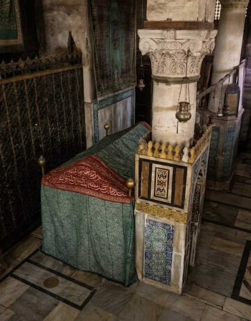 MuslimLandmarks's tweet photo. 📍 The House of Fāṭimah (رضي الله عنها) – Inside the Sacred Chamber, al-Masjid an-Nabawī, Madinah

This spot lies within the golden grilles that surround the Prophet's ﷺ resting place, and it is all that remains of the home of his youngest daughter, Fāṭimah az-Zahrāʾ (رضي الله عنها), and her husband ʿAlī ibn Abī Ṭālib (رضي الله عنه).

Their home stood directly north of the room of ʿĀʾishah رضي الله عنها, where the Prophet ﷺ is buried. The two homes were separated only by a wall, so the Prophet ﷺ was always within a few steps of his daughter.

In 88–91 AH / 707–710 CE, ʿUmar ibn ʿAbd al-ʿAzīz (رحمه الله) rebuilt the mosque on the orders of the caliph al-Walīd, and the Prophet's ﷺ wives' apartments were brought into the building. Part of Fāṭimah's (رضي الله عنها) house went inside the new five-sided wall around the Prophet's ﷺ resting place.

Today the site is inside the grille enclosure put up by the Mamluk Sultan Qāytbāy after the great fire of 886 AH / 1481 CE. The door on the eastern side of the enclosure is still called Bāb Fāṭimah, the Door of Fāṭimah.

Behind the house, on its northern side, the Prophet ﷺ is reported to have spread a mat at night and prayed Tahajjud. That spot was later marked as the Miḥrāb at-Tahajjud. 

The cloth-draped structure is known as Sarīr Fāṭimah, "the Bed of Fāṭimah". It is not a grave. It is a raised, box-like structure dressed in the same green-and-red kiswah style used inside the Sacred Chamber.

For centuries it served a practical purpose. Gifts sent to the Prophet's ﷺ Mosque by sultans, royal women and dignitaries (lamps, silver and gold) were stored in chests beneath it. Much of this treasury was taken to Istanbul in the Ottoman era and is now in the Topkapı Palace collections.