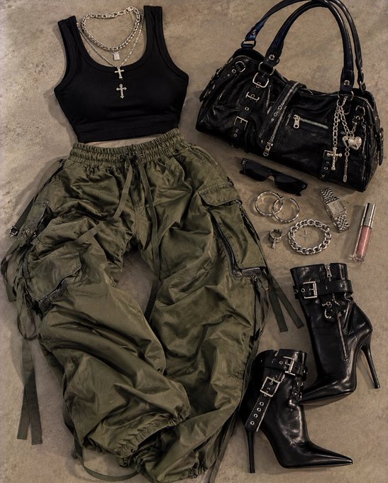 A flat lay outfit featuring a black cropped tank top, olive green cargo parachute pants, black buckled high-heel boots, a black leather handbag, and silver cross jewelry.