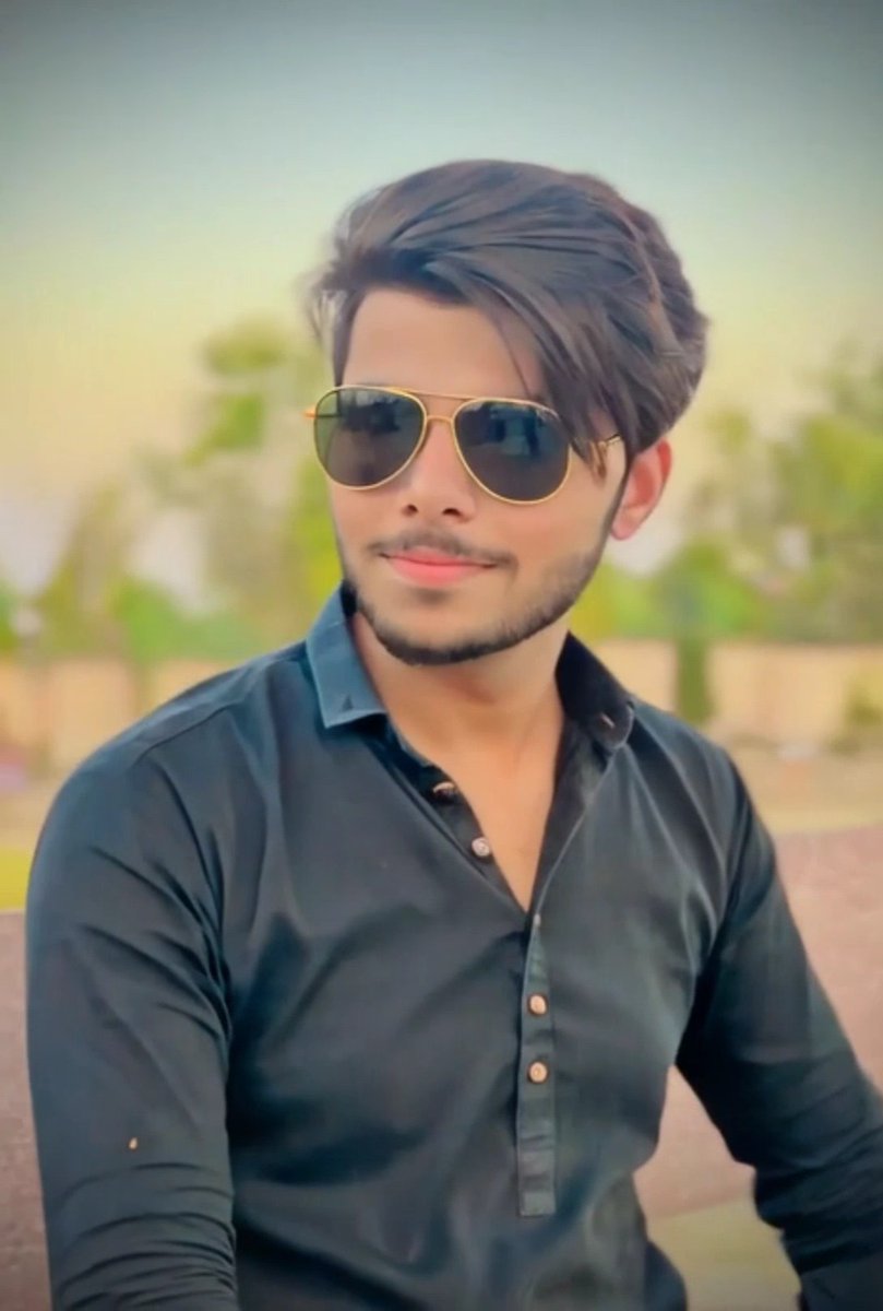 A portrait of a young man with styled hair, a beard, and aviator sunglasses wearing a black button-up shirt.