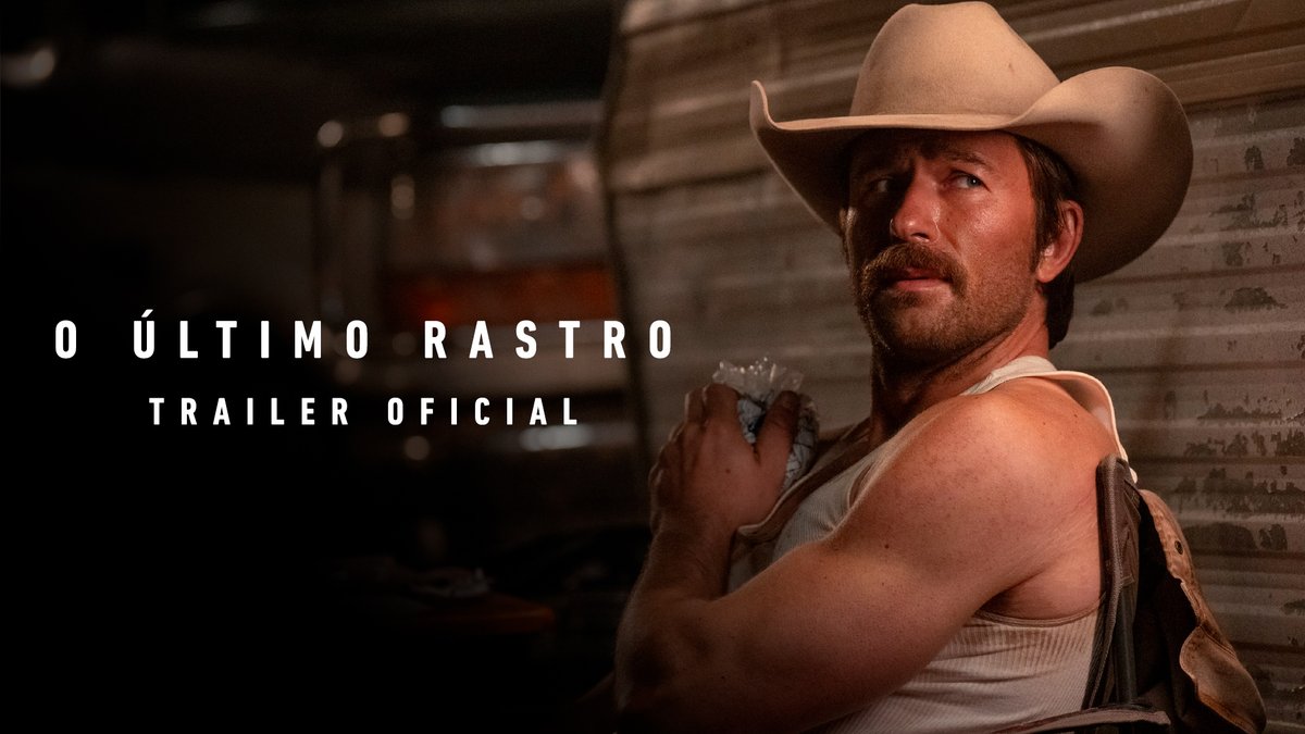 A man in a cowboy hat and white tank top looks back over his shoulder in a dimly lit setting, with the Portuguese text "O ÚLTIMO RASTRO - TRAILER OFICIAL" displayed on the left. The image serves as promotional material for the official trailer of "The Last Trail," featuring star Brandon Sklenar, whose rugged appearance reinforces the film's intense, determined tone.