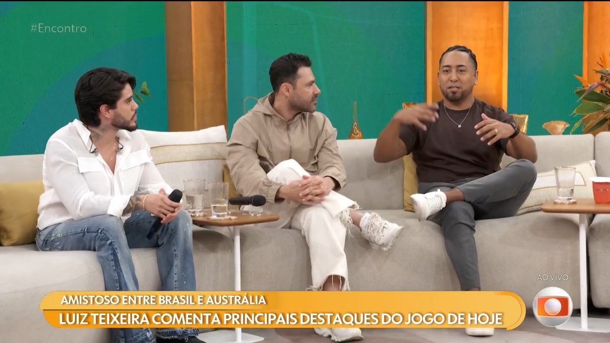 Three men sitting on a couch on the Brazilian TV show 'Encontro' discussing the friendly match between Brazil and Australia, with commentary by Luiz Teixeira about today's game highlights.