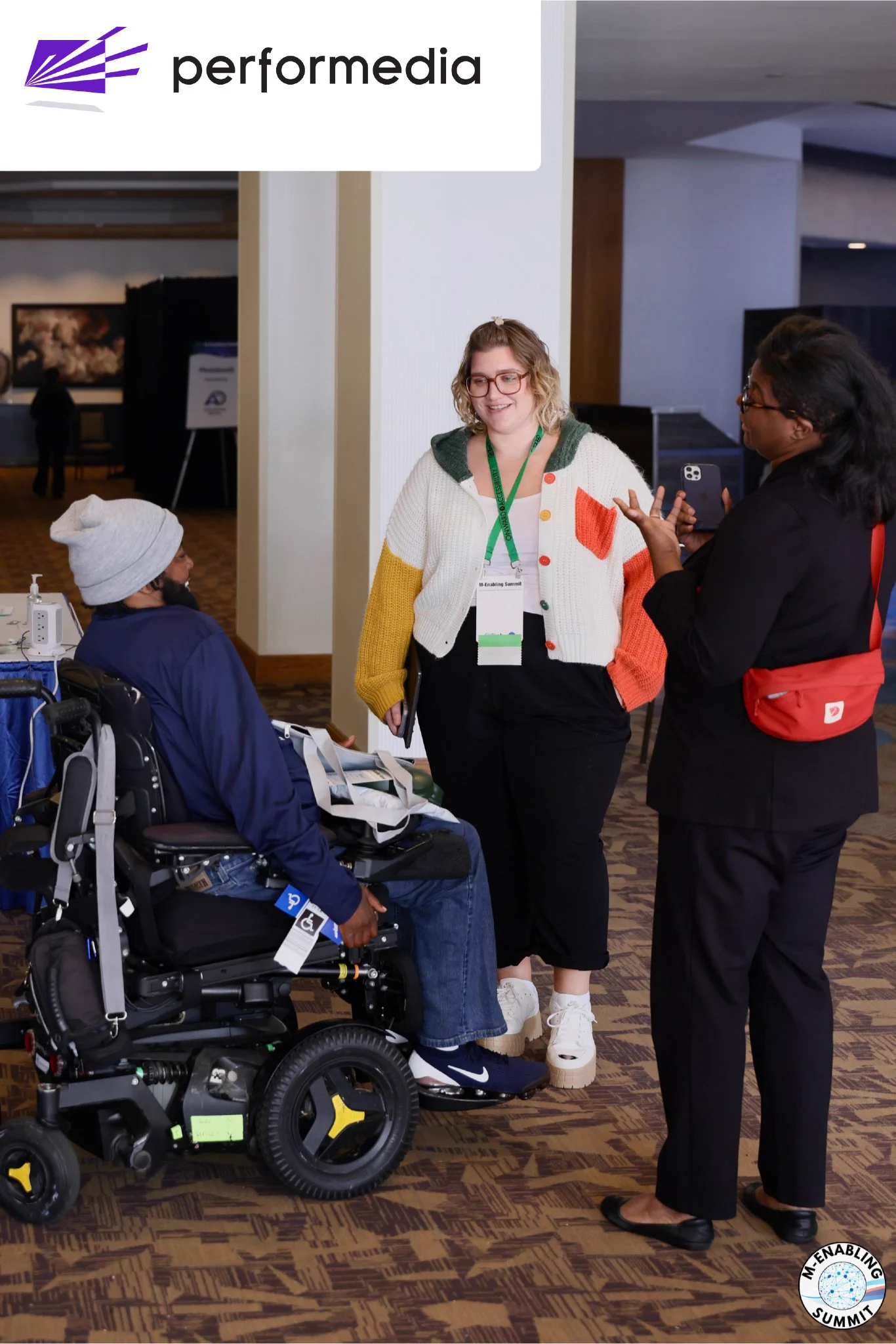 Attendees engaging with each other at the 2025 M-Enabling Summit. At the top left is a white logo banner with the Performedia logo.