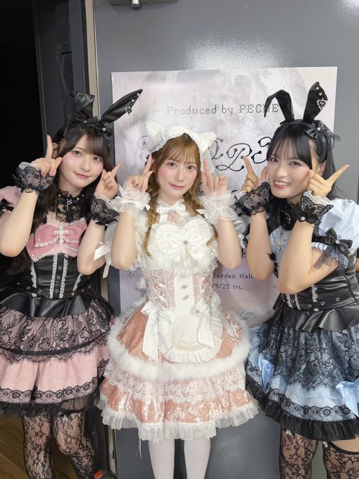 Three young women pose playfully with bunny ears and peace signs in elaborate Lolita fashion outfits—one in pink and black, one in a cream and white maid-style dress, and one in light blue and black—in front of a poster reading "Produced by PECHE" for the "Malymoon Halloween Fashion Show 2026" at Garden Hall on 10/25. The image captures the celebratory atmosphere of the Halloween fashion event where the members of Igiyaruzoku Tohoku-San gathered with performer Mie Higashimura.