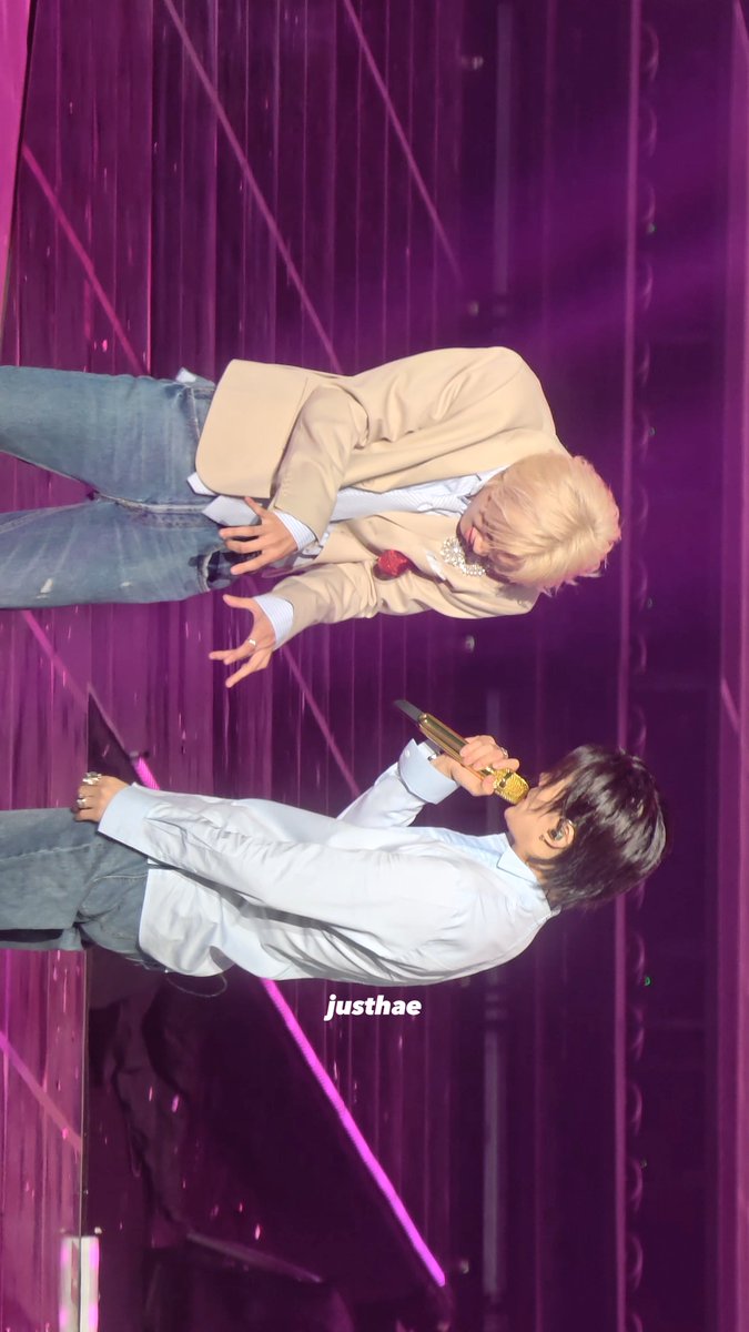 Two performers share a playful moment on a purple-lit stage—one with blonde hair in a beige blazer holding a microphone and making a peace sign, while the other in a light blue shirt sings into a gold microphone—capturing the fun "sea otter" energy referenced in the post about Haechan and Yuta. The watermark "justhae" appears in the center of the image.