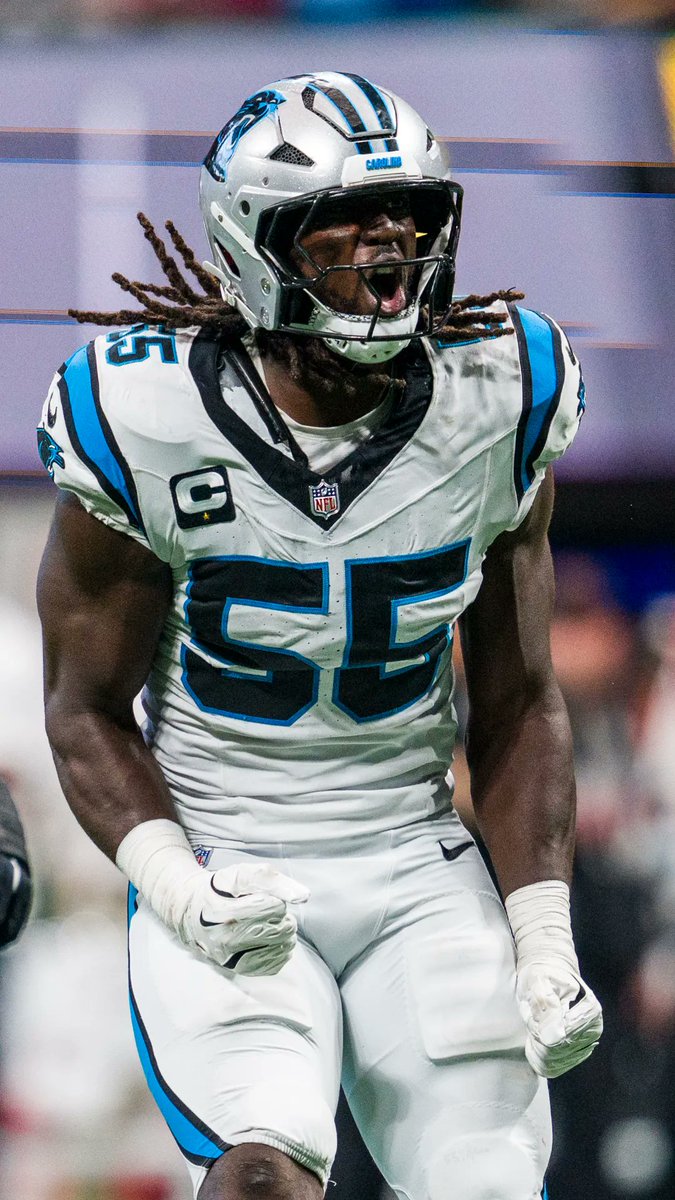 Carolina Panthers linebacker #25, wearing the captain's "C" patch on his white away jersey, celebrates intensely with clenched fists and an open-mouthed yell during a game. The image of the All-Pro defender aligns with the post about Devin Lloyd discussing his military family upbringing on the "Football Unfiltered" podcast.