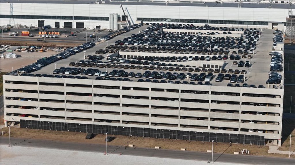 JoeTegSpaceX's tweet photo. This is something new, at least at this SCALE, at Giga Texas … hundreds of vehicles, Model Y’s, @cybertruck &amp; Cybercabs being move from the W outbound lot to the E parking garage, filing up inside and on the roof! https://t.co/4NbOuujROz