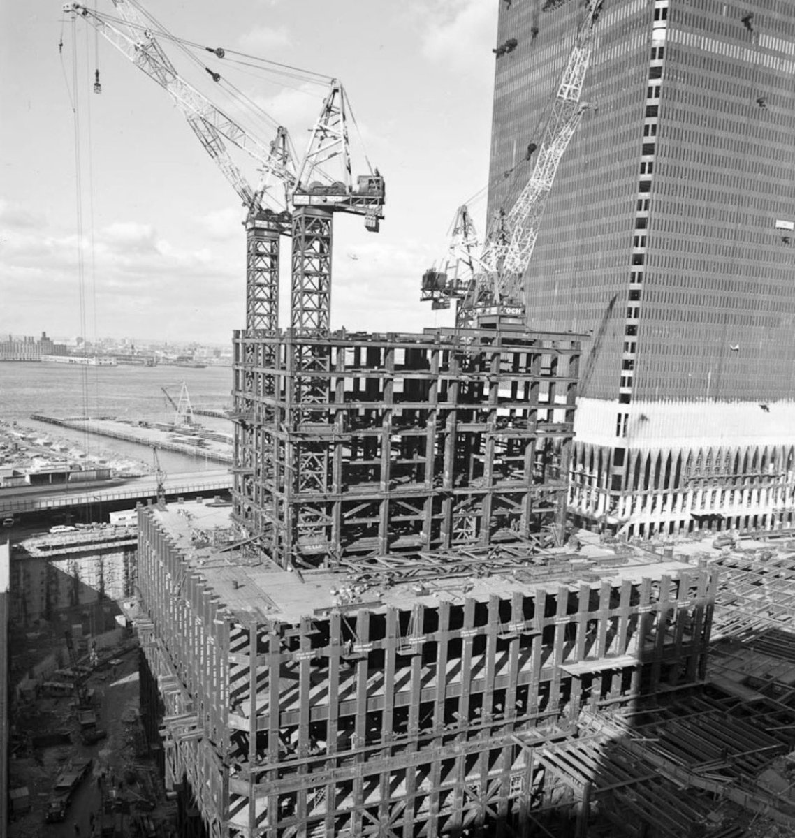 JackMedia7's tweet photo. 🔥 NO PLANES WERE USED ON 9/11! NO PLANE WOULD BE ABLE TO FLY COMPLETELY THROUGH AND "HOT KNIFE THROUGH BUTTER," SPEED AND HAVE THE NOSE EXTEND THROUGH THE OTHER SIDE! 
COURTESY OF @JACKMEDIA7 

🔥 READ THIS! 

🔥 The photo is from original World Trade Center construction around 1970. The finished-looking tower on the right is the North Tower with cladding going on; the open steel cage in the foreground is the South Tower rising. Almost everything you can see in the unfinished structure is steel. Concrete is present, but most of it is either below grade or not yet poured on these floors.

🔥 Steel — the load-bearing system you see.

🔥 The towers used a framed-tube design rather than a conventional interior grid of columns. Gravity load was shared roughly equally between a stiff perimeter “tube” and a central steel core. Wind load was carried almost entirely by the perimeter.

🔥 Perimeter tube:** From about the 10th floor up, each face had 59 closely spaced built-up box columns (236 total around the square plan). Adjacent columns were tied at every floor by deep steel spandrel plates (typically about 52 in. deep). Three columns plus their connecting spandrels were shop-fabricated as three-story wall panels, then stacked and welded on site. That is the dense vertical grid visible in the photo. Column plate thickness and steel grade varied with height and location (yield strengths from about 42 ksi to 100 ksi) so the tube could take both gravity and wind without wasting material.
Core:** A rectangular service core of large steel box columns and wide-flange columns carried elevators, stairs, and mechanical shafts. The heaviest base sections were multi-story pieces set on steel grillage and concrete on Manhattan schist.
Floors:** Prefabricated steel trusses (roughly 36 ft or 60 ft long) spanned from core columns to the perimeter wall. They supported corrugated metal deck. Those trusses also helped stabilize the columns. A hat truss at the roof later tied core and perimeter together.

🔥 The complex used on the order of 200,000 tons of structural steel. Prefabrication of wall panels and floor units is why the skeleton could rise several floors a week once steel erection was underway.

🔥 Concrete — foundation, floors, and the “bathtub”

🔥 Concrete is less obvious in this shot because the South Tower is still a bare frame.

🔥 Slurry-wall foundation (“bathtub”):** Because the site was landfill next to the Hudson, a continuous reinforced-concrete retaining wall was built first. Trenches were filled with bentonite slurry, steel cages were lowered in, then concrete was tremied from the bottom, displacing the slurry. That wall held back groundwater so the site could be excavated about 70 ft to bedrock.
Foundations:** Core and perimeter loads went to steel grillage on concrete footings bearing on schist.
Floor slabs:** After the steel trusses and metal deck were in place, workers poured lightweight concrete — typically about 4 in. on 1½-in. deck outside the core and about 5 in. in the core. The slab acted compositely with the steel. Those pours had not yet happened on the open floors in the photo. The neighboring North Tower already has cladding, so its lower floors would already have slabs.

🔥 The whole World Trade Center complex used roughly 425,000 cubic yards of concrete. In this particular image, though, the dramatic visual is the steel tube and core; the concrete work is either already in the ground or waiting for the next cycle of decking and pours.

🔥 MORE 9/11 TRUTH AT THE WORLD'S CONNECTION TO UNSTOPPABLE TRUTH AT 17PLUS WORLDWIDE TRUTH NETWORK AT https://t.co/GmUOATMVLF
